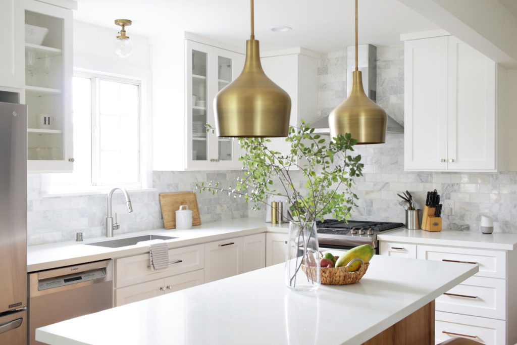 white kitchen with marble backsplash and gold pendants